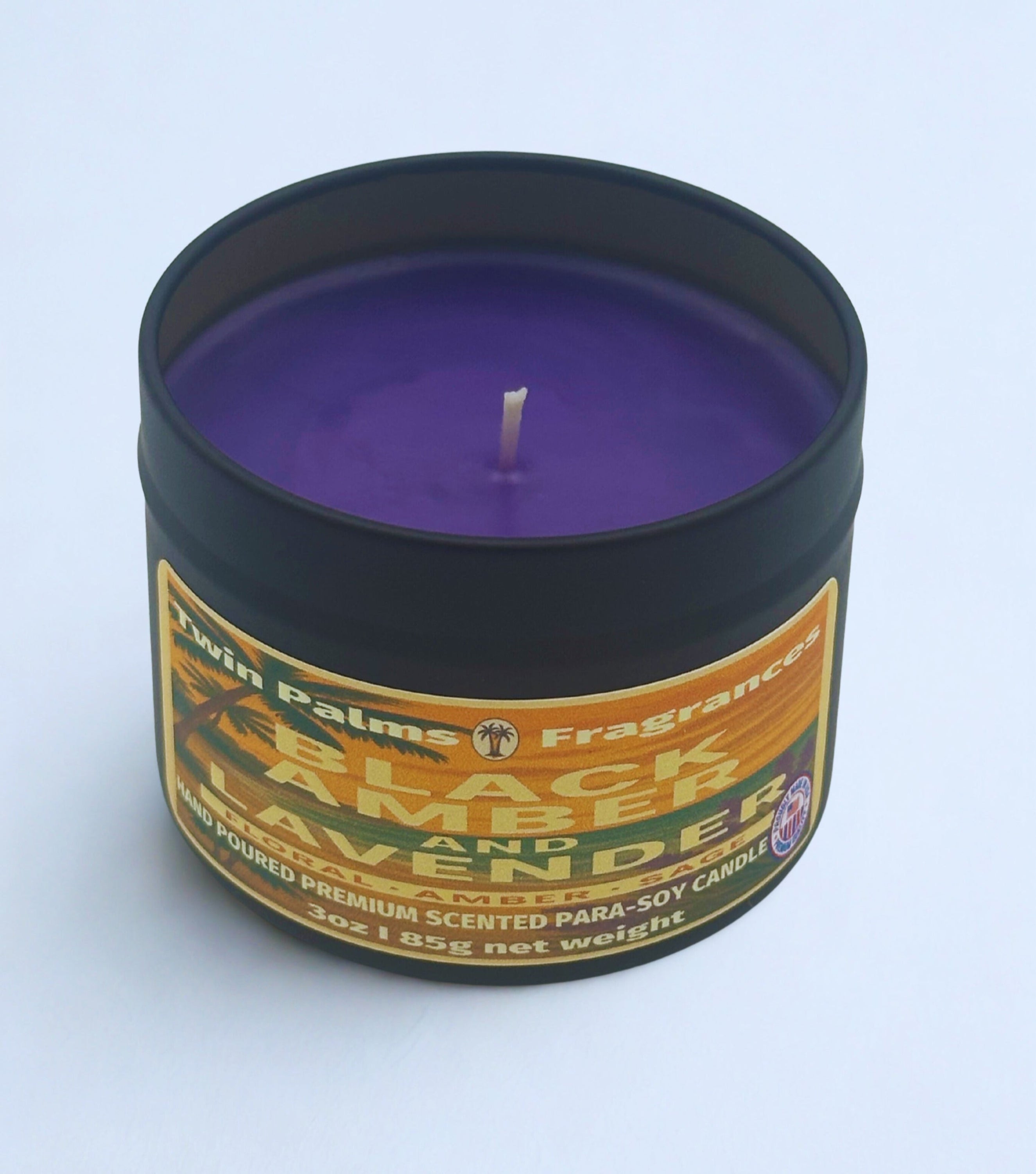 Candle in a tin labeled 'Black Amber and Lavender' by Twin Palms Fragrances on a light blue background.