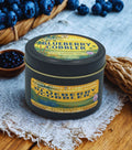 Tin of 'Blueberry Cobbler' candle with blueberries around on a wooden surface