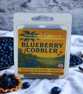 Twin Palms Fragrances Blueberry Cobbler wax melt packaging with blueberries and a pie in the background.