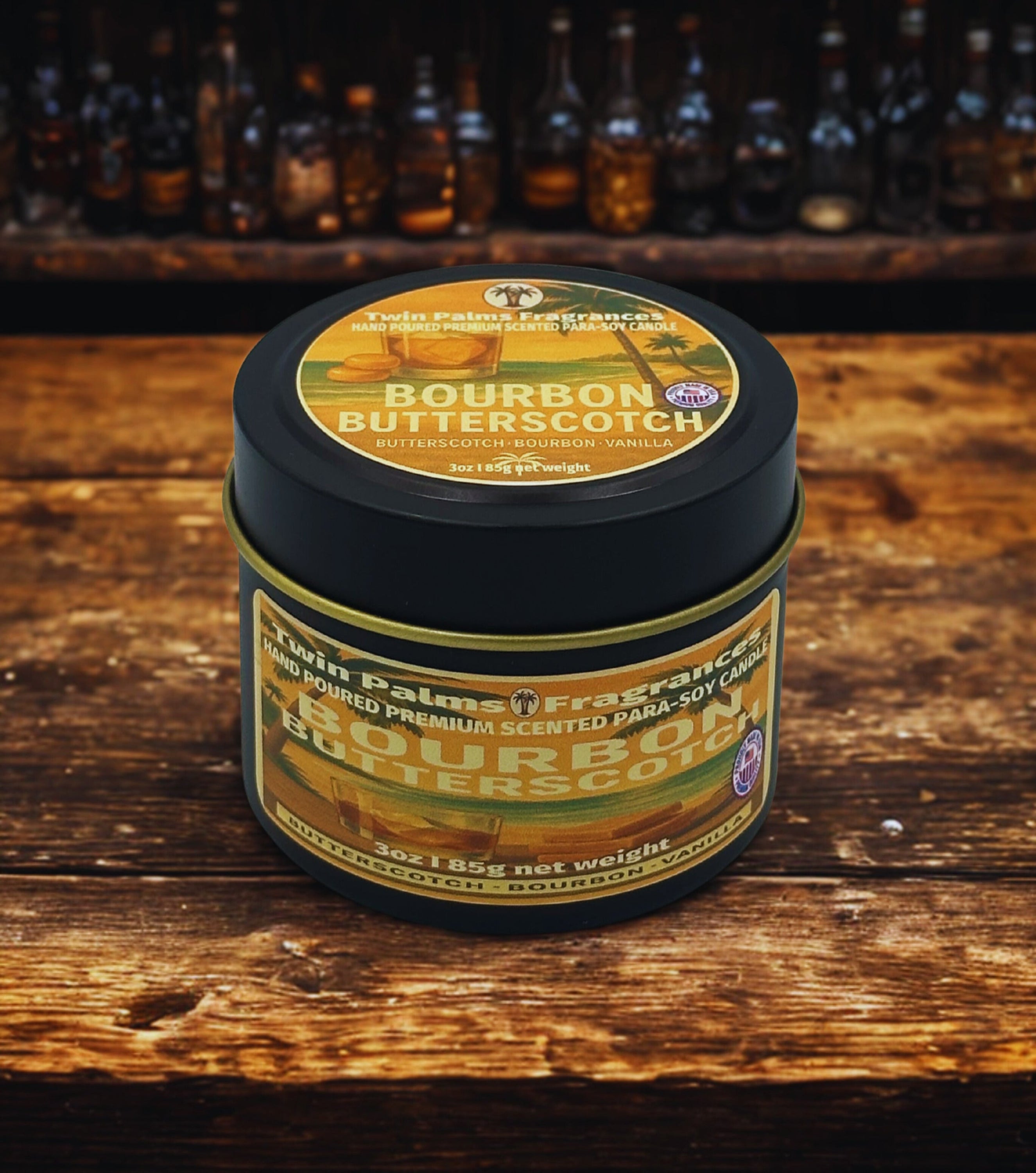 Tin of Twin Palms Fragrances Bourbon Butterscotch candle on a wooden surface with bottles in the background