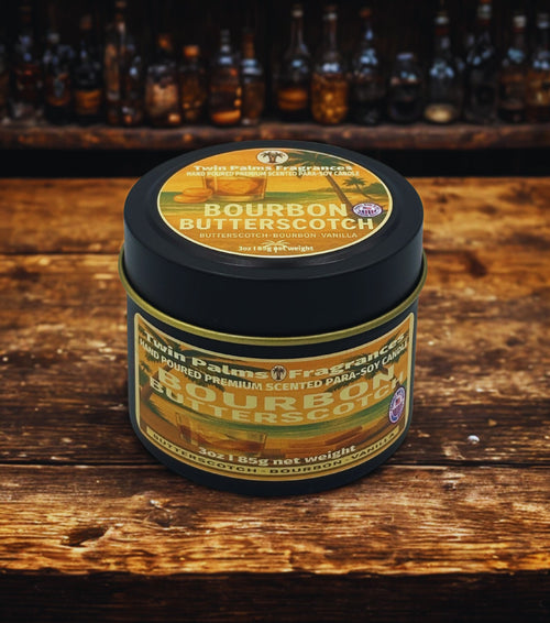 Tin of Twin Palms Fragrances Bourbon Butterscotch candle on a wooden surface with bottles in the background