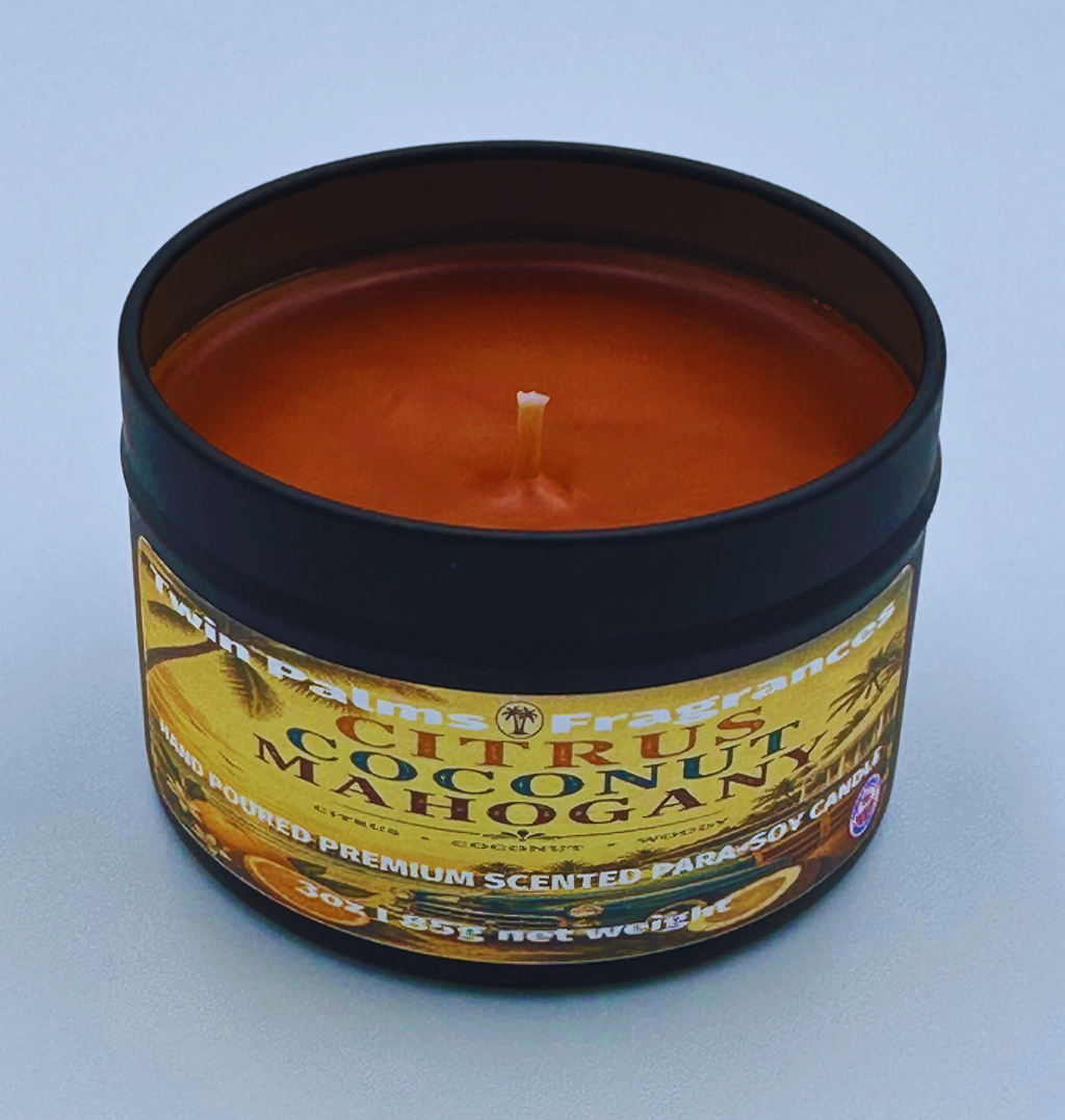 Candle in a tin labeled 'Citrus Coconut Mahogany' by Twin Palms Fragrances on a light blue background.