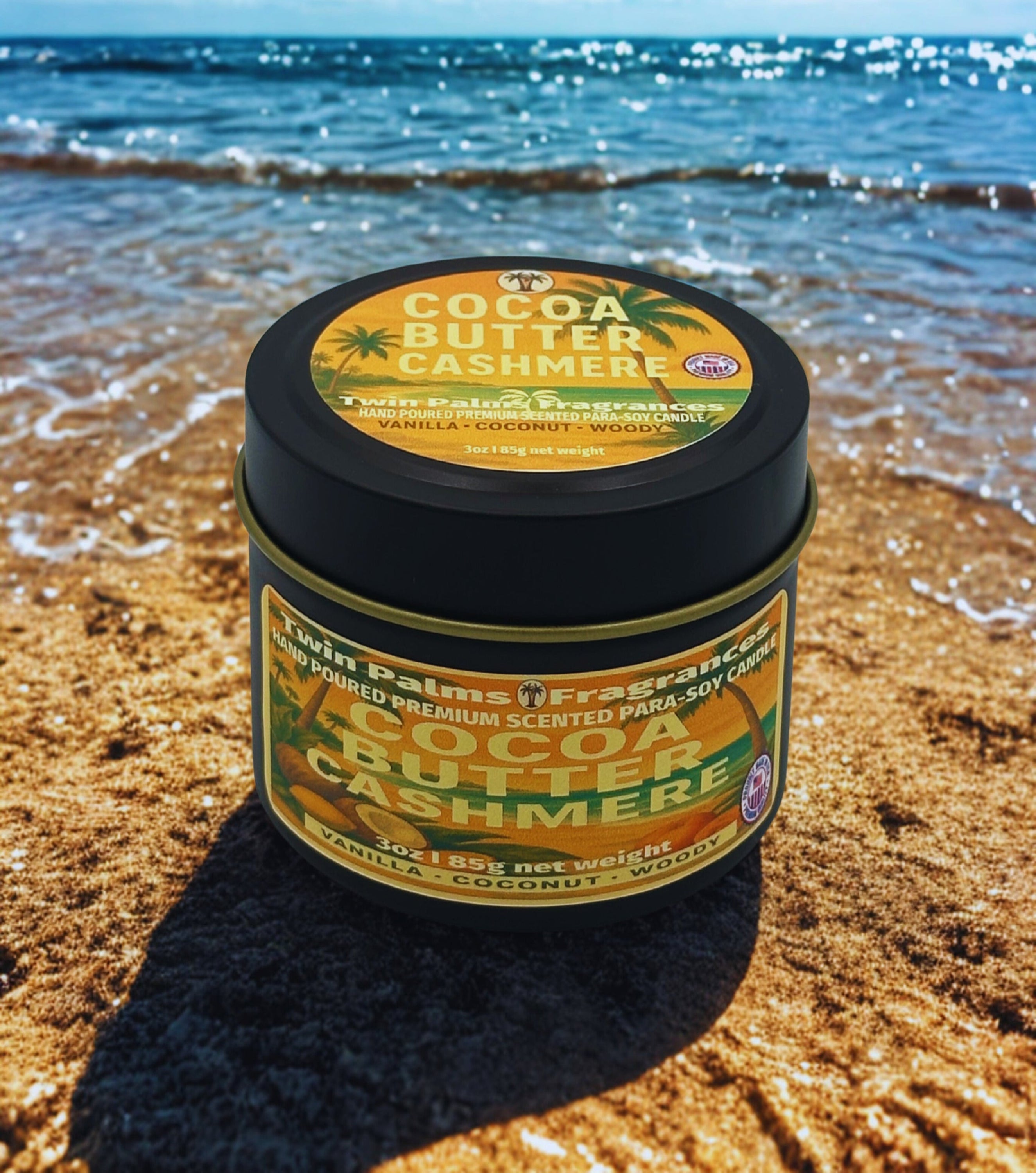 Twin Palms Fragrances Tin of Cocoa Butter Cashmere candle on a sandy beach with ocean in the background