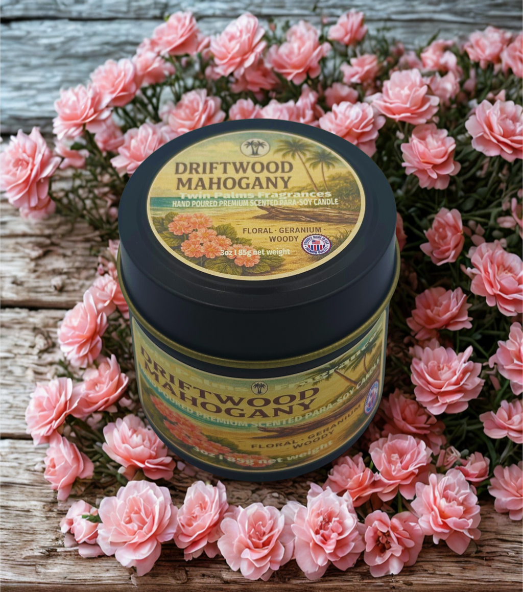 Candle tin labeled 'Driftwood Mahogany' surrounded by pink flowers on a wooden surface