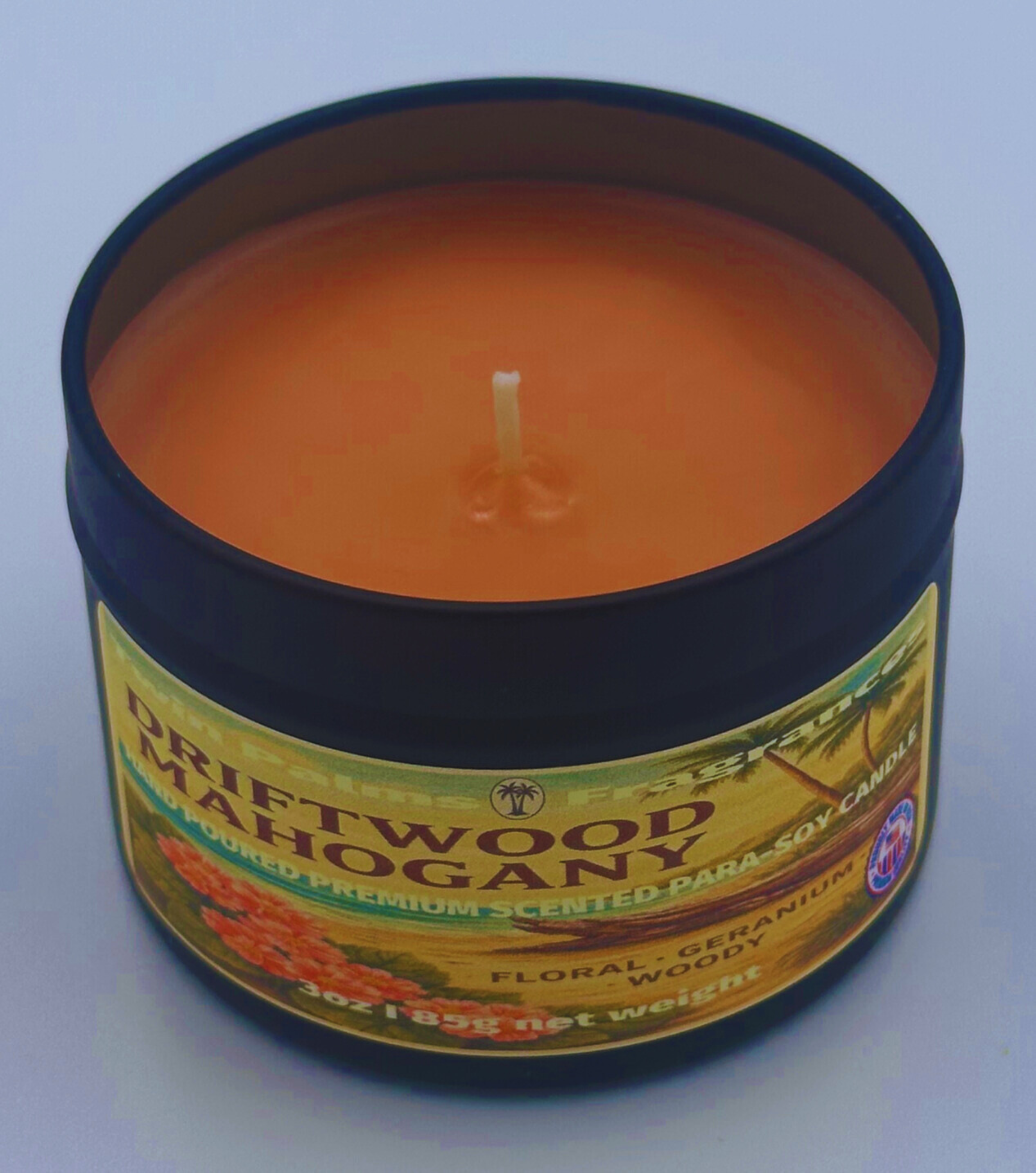 Candle in a tin labeled 'Driftwood Mahogany' on a light blue background