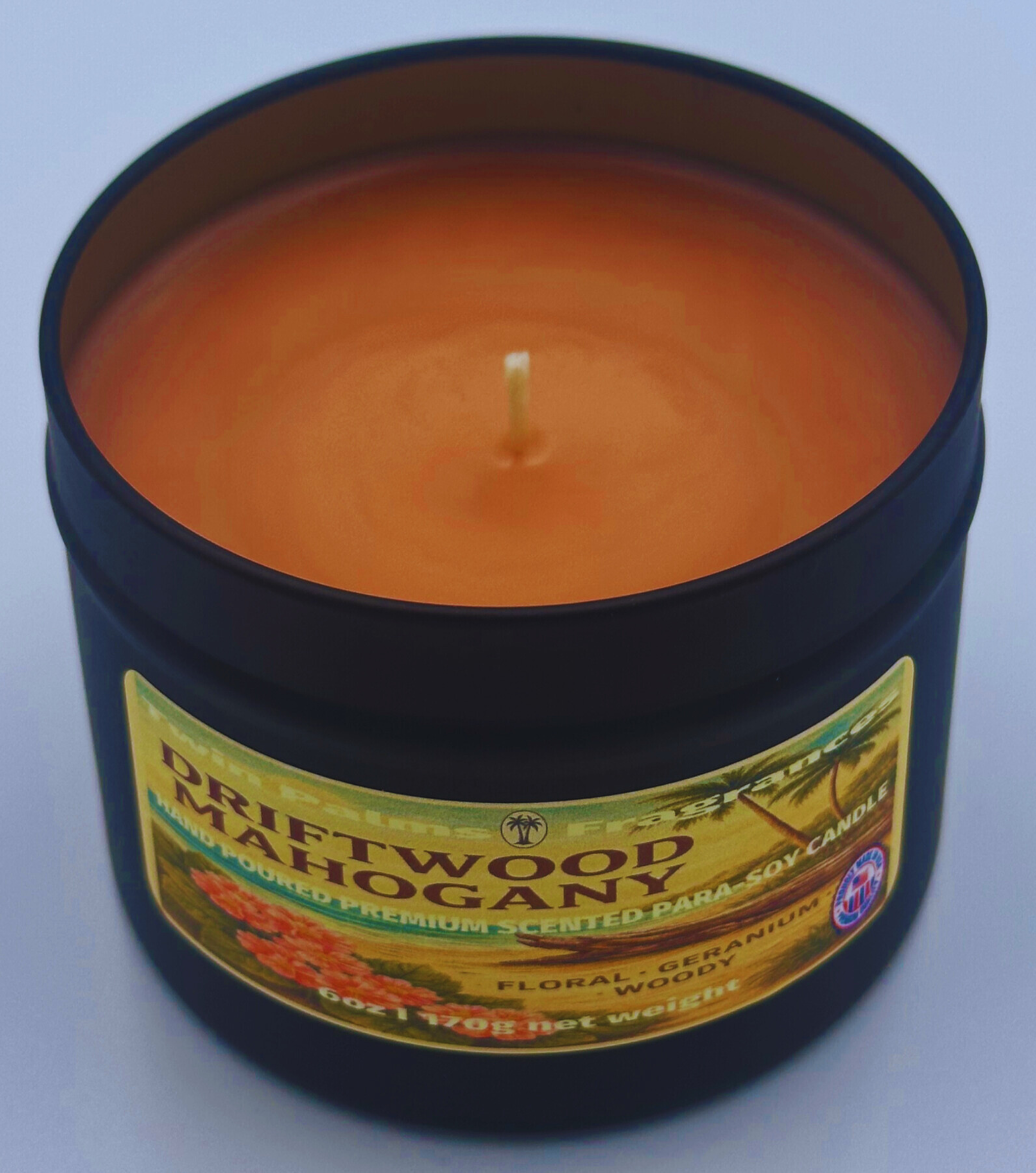 Candle in a tin labeled 'Driftwood Mahogany' on a light blue background