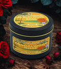 Twin Palms Fragrances Sandalwood Rose candle in a black tin with a yellow label on a wooden surface surrounded by red roses.