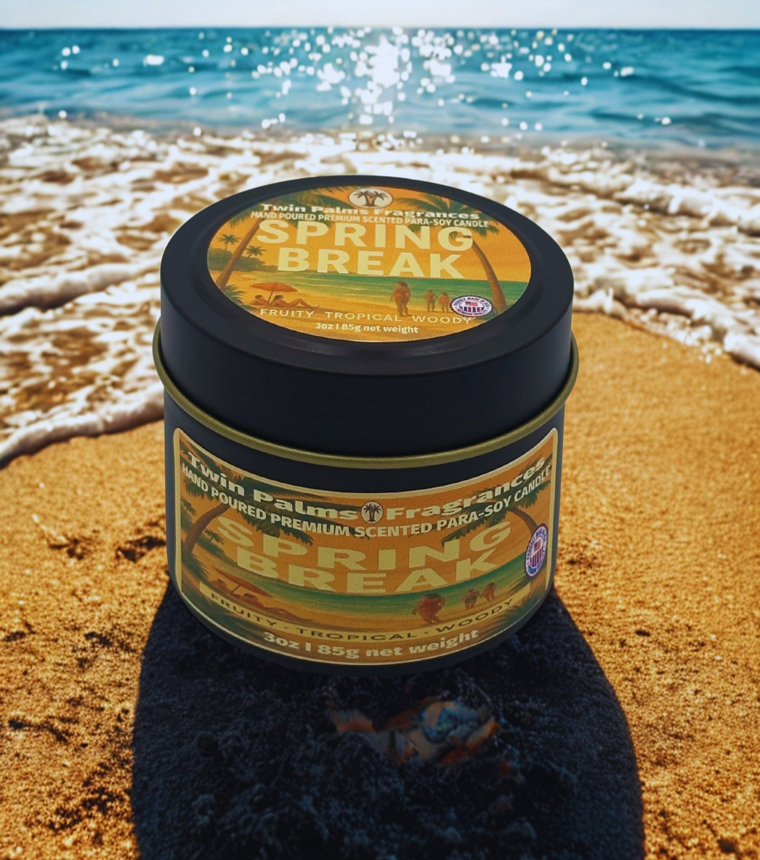 Candle tin labeled 'Spring Break' by Twin Palms Fragrances on a beach with ocean waves.