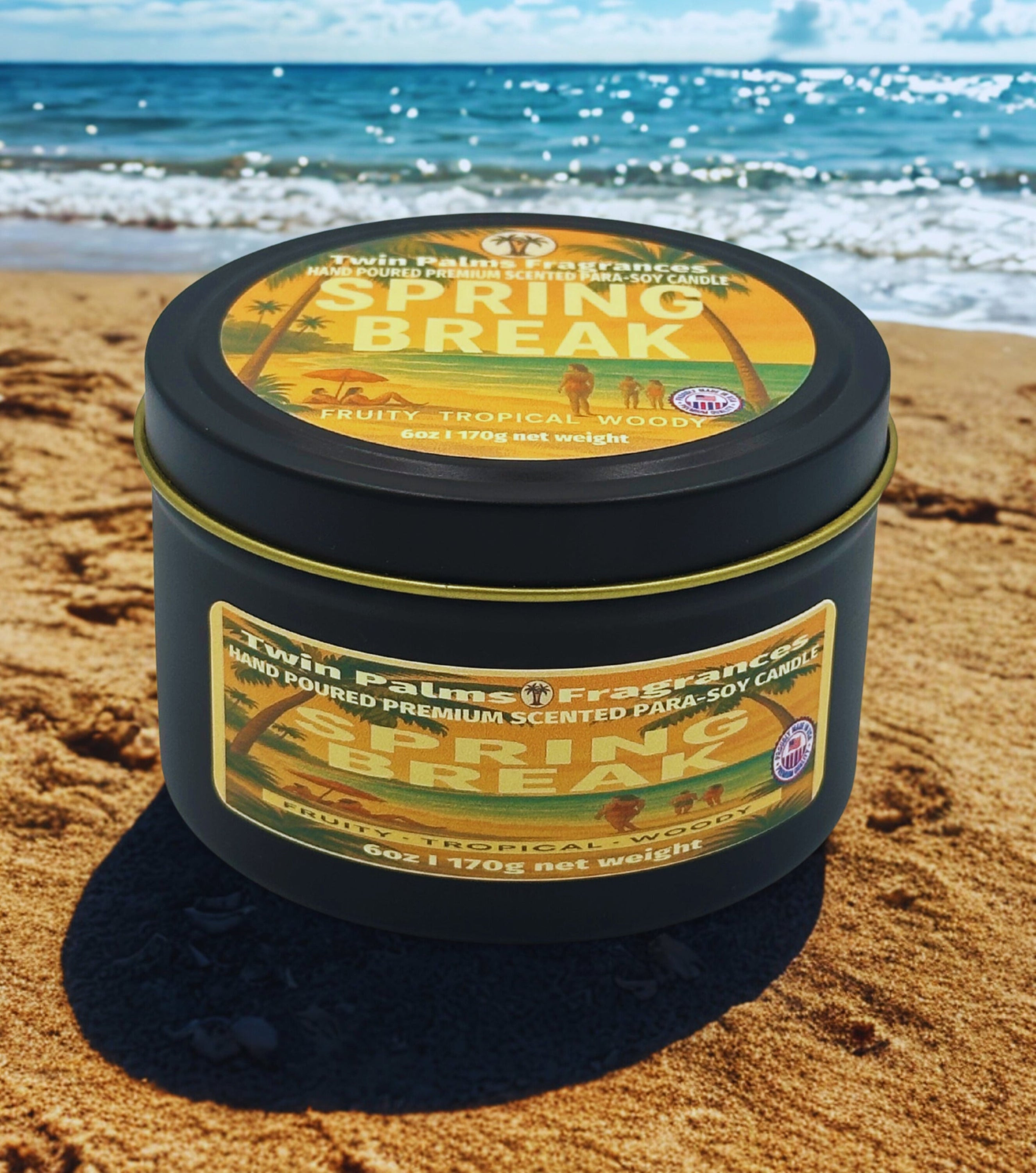 Twin Palms Fragrances candle tin labeled 'Spring Break' on a sandy beach with ocean in the background