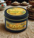 Twin Palms Fragrances Tea time scented candle in a black tin with decorative label on a textured surface.
