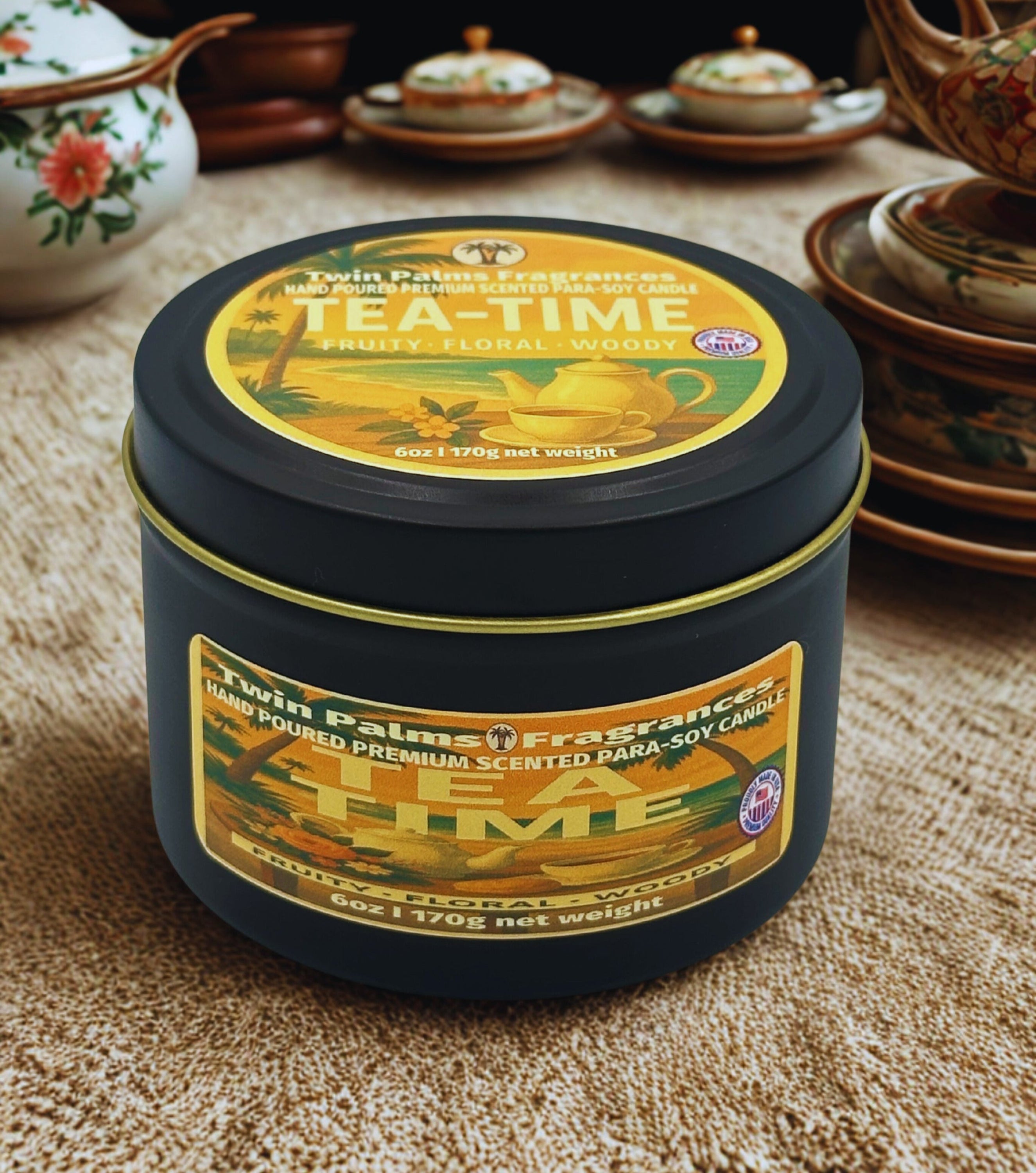 Twin Palms Fragrances Tea time scented candle in a black tin with decorative label on a textured surface.