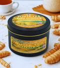 Twin Palms Fragrances White Tea and Ginger candle in a tin surrounded by croissants on a white surface
